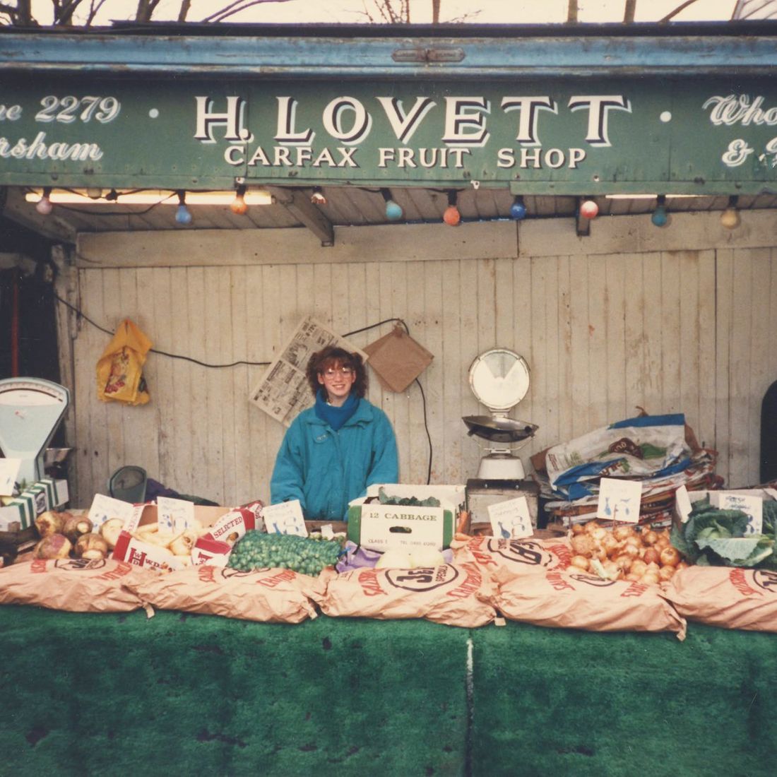 A young woman behind H. Lovett's fruit and veg stall