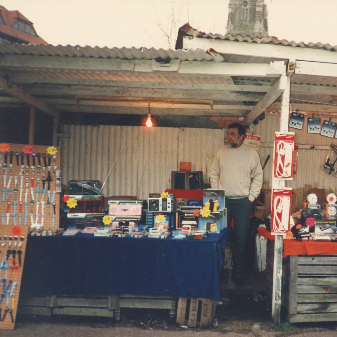 A trader with radios and watches under a tin-roofed market stall